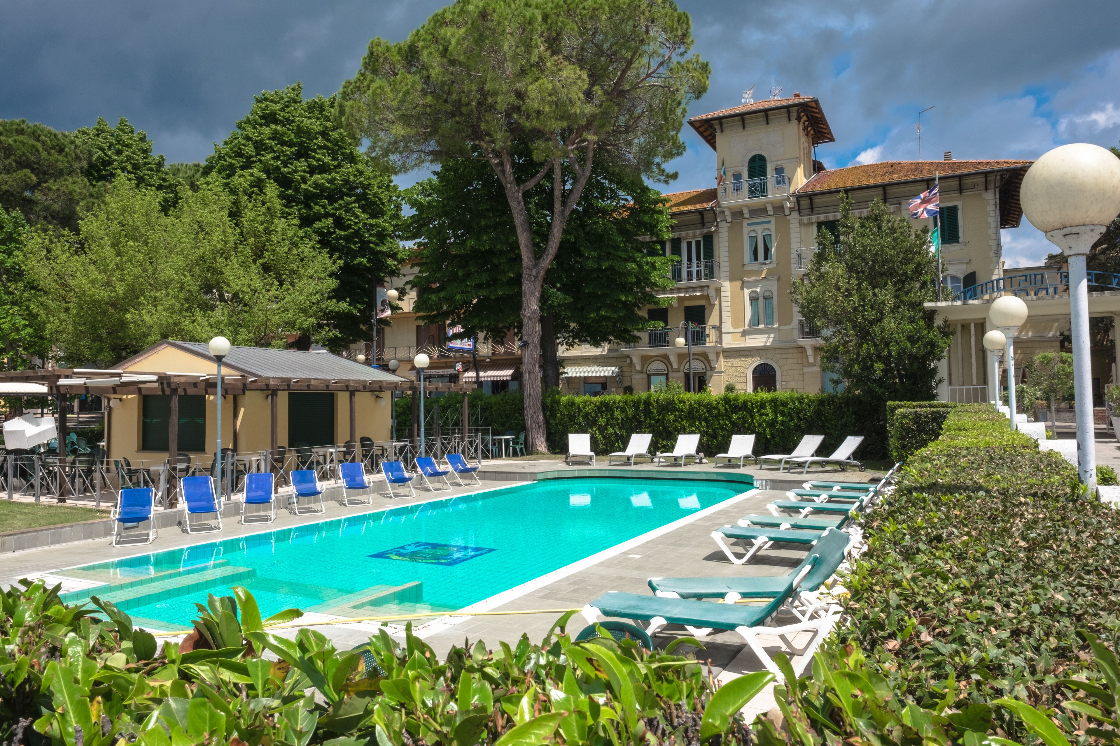 A swimming pool with lounge chairs, surrounded by greenery and a building with balconies.