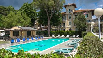 A swimming pool with lounge chairs, surrounded by greenery and a building with balconies.