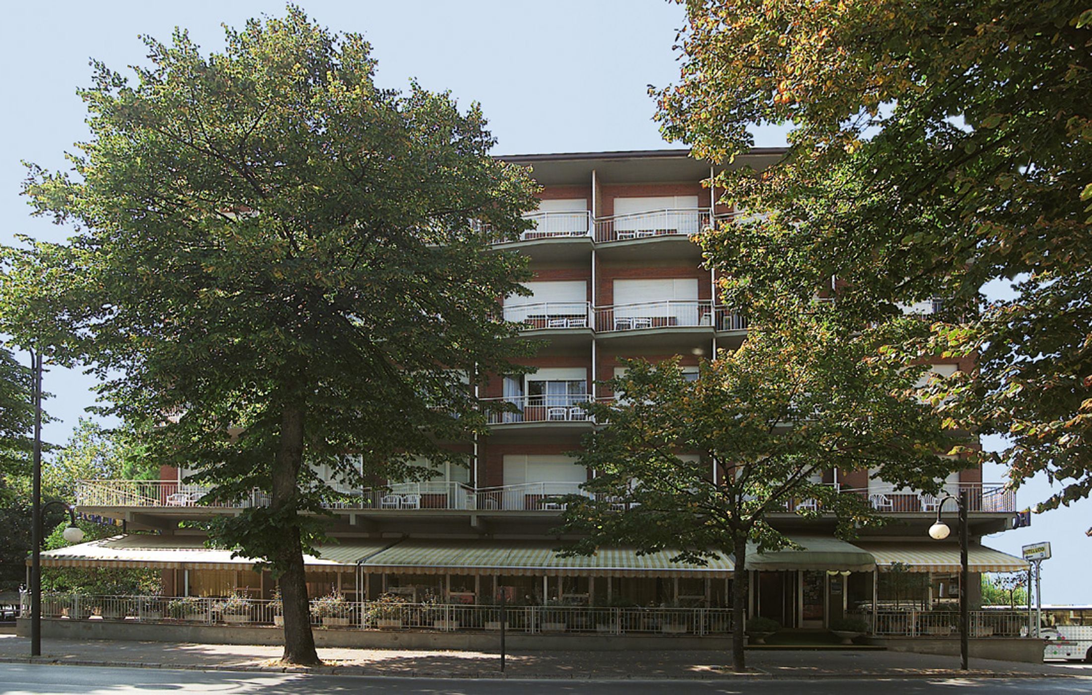 Un edificio a più piani con balconi, una zona relax all'aperto coperta e un albero in primo piano.