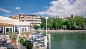 Un restaurante frente al agua con terraza, vista al río y edificios al fondo.