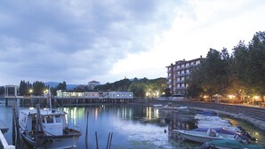 Un puerto deportivo con barcos amarrados, un edificio frente al agua y un paisaje urbano al fondo.