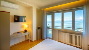 Habitación de hotel con cama, escritorio con lámpara, televisión y ventana con vista al mar.