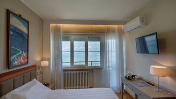 Una camera d'albergo con un letto, una scrivania, una TV, una finestra vista mare e un condizionatore.