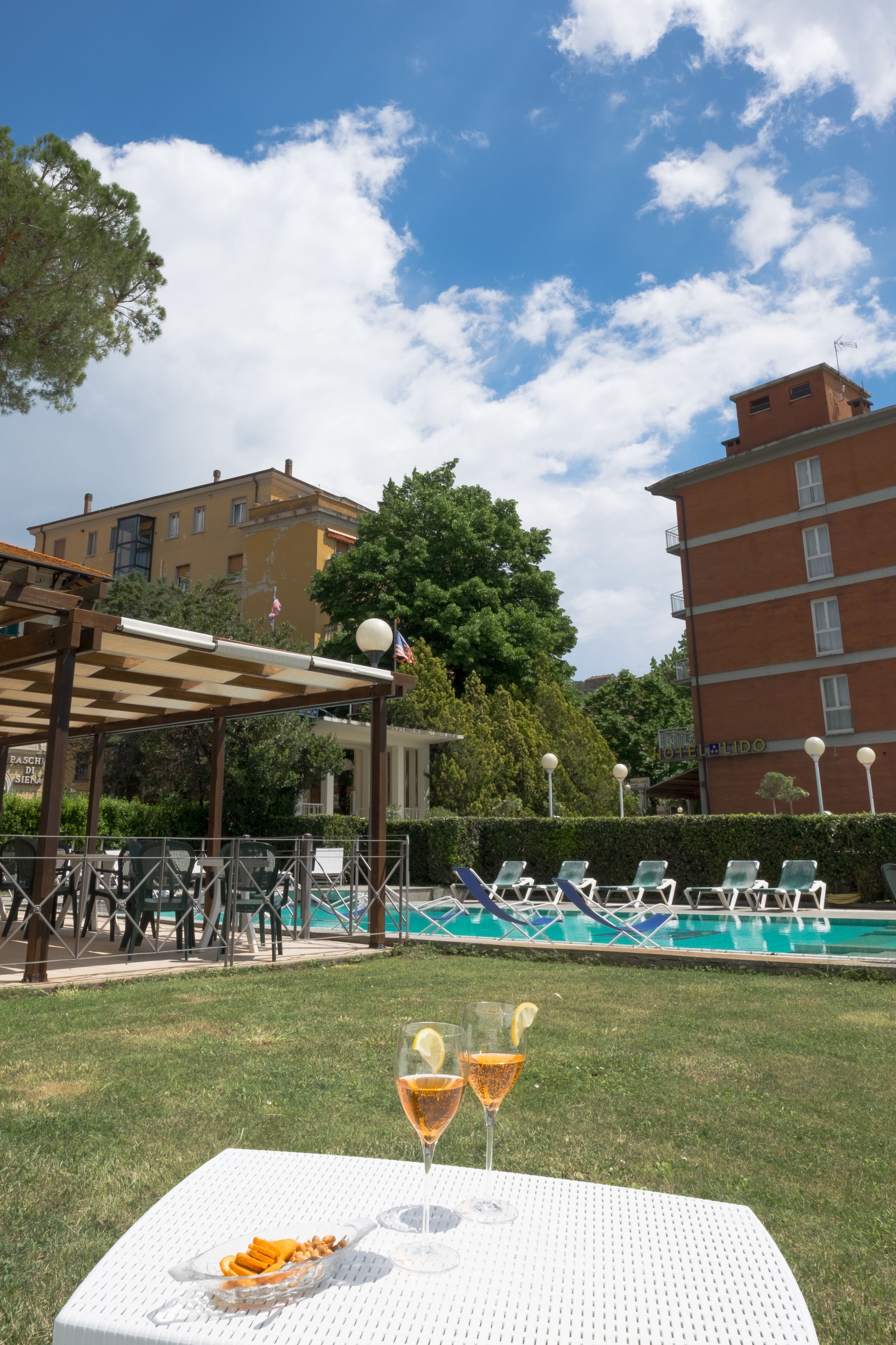 Zona de piscina amb gandules, una taula amb aperitius i begudes, i vista d'un edifici amb un rètol que diu "HOTEL LANDO".
