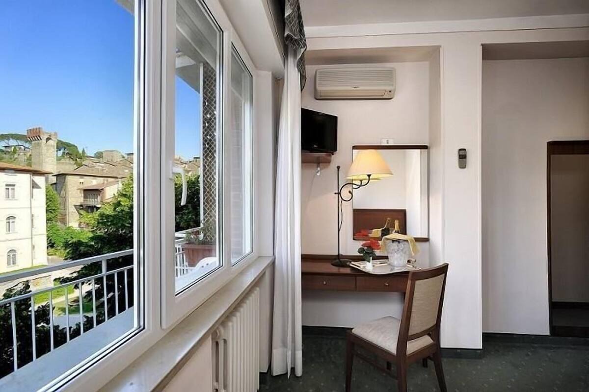 Ett hotellrum med en balkong, ett skrivbord med en stol, en lampa och en tv.