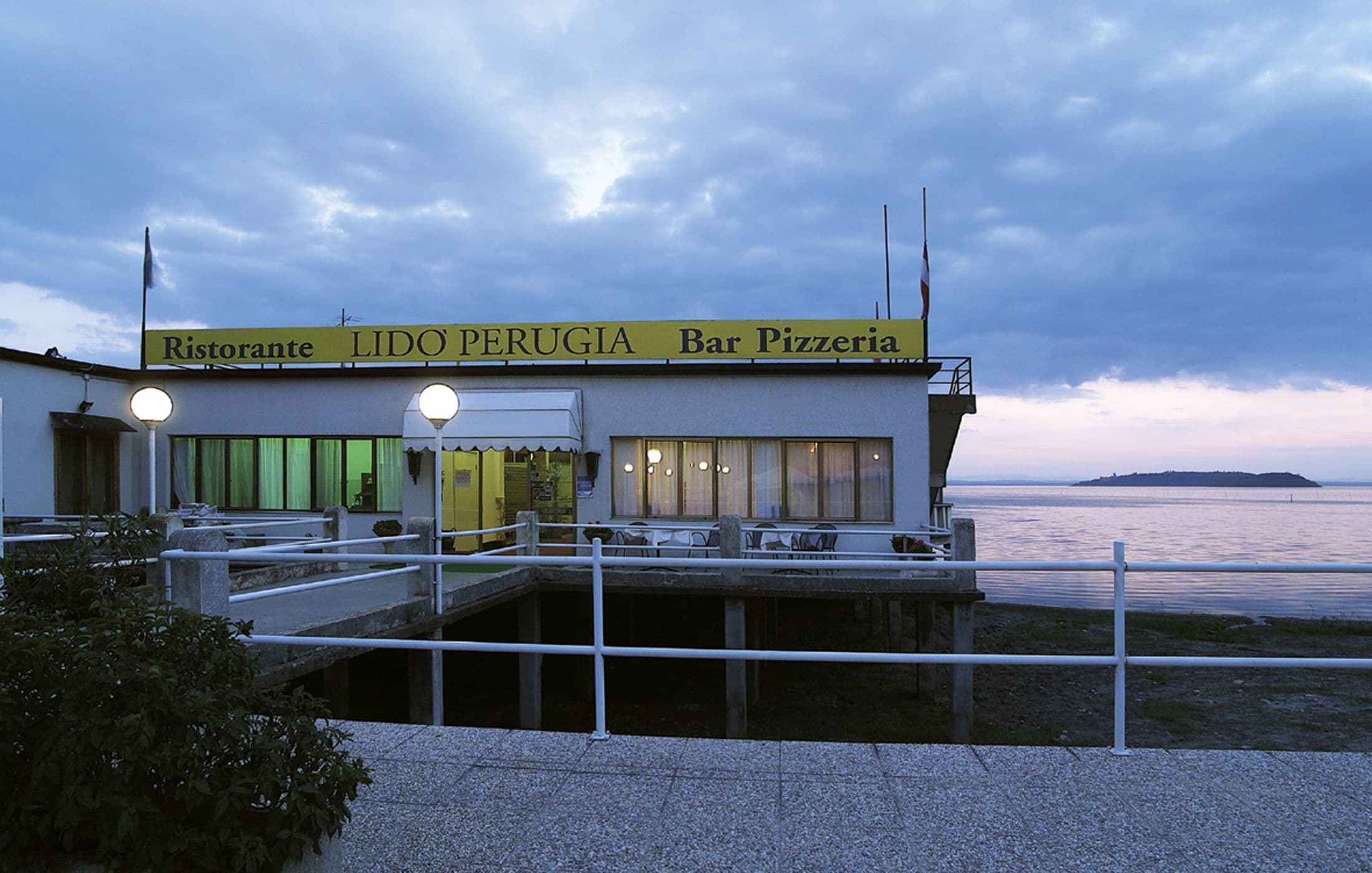 A waterfront bar and restaurant named 'Ristorante LIDO PERUGIA Bar Pizzeria' with outdoor seating and a view of the water.