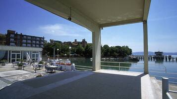 Un espacio al aire libre con mesas y sillas, con vista a un cuerpo de agua con barcos y un muelle.
