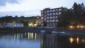 Un hotel frente al río con varios balcones, un río tranquilo y un muelle con barcos.