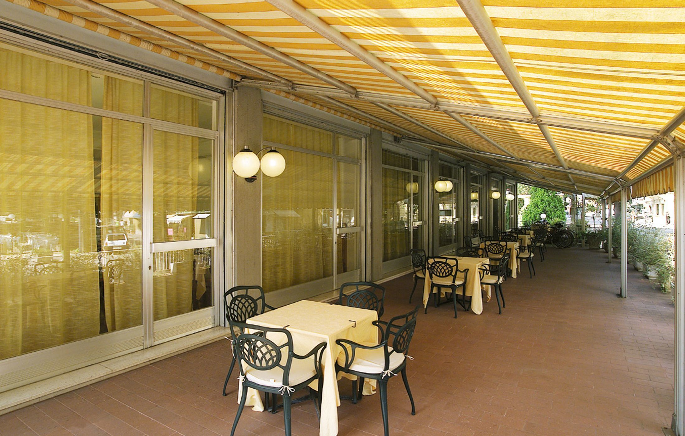 An outdoor covered patio area with tables and chairs, large windows, and a striped canopy.