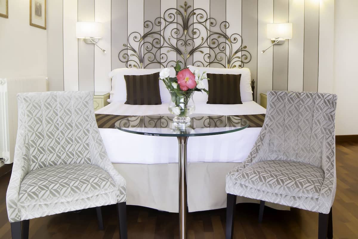 Une chambre d’hôtel avec un lit, deux fauteuils à motifs, une table en verre et un élément décoratif mural.