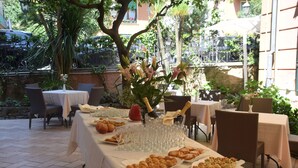 An outdoor dining area with tables set for a meal, surrounded by greenery and a stone wall. - Hotel Jolanda (Santa Margherita Ligure)