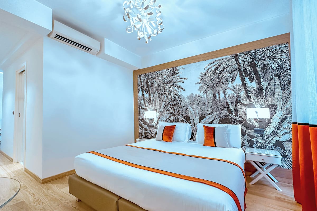 Une chambre d’hôtel moderne avec un grand lit, un bureau et une fresque représentant une végétation tropicale sur le mur.