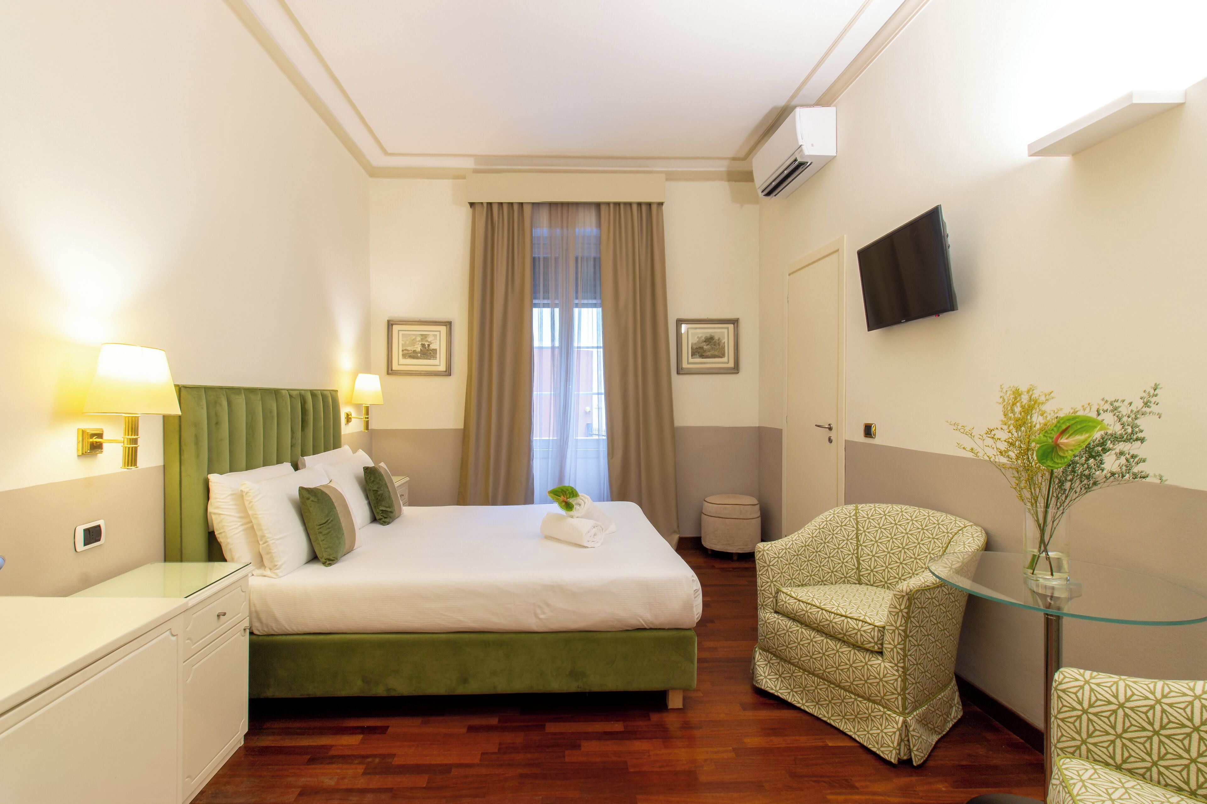 Ein Hotelzimmer mit Bett, Stuhl, kleinem Tisch, Fernseher und einem Fenster mit Vorhängen.