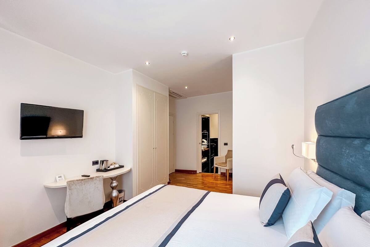 Une chambre d’hôtel moderne dotée d’un grand lit, d’un téléviseur à écran plat fixé au mur, d’une table de chevet et d’un dressing.