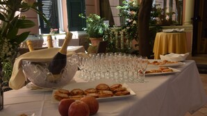 A table set with champagne, glasses, and pastries in a room with potted plants and a yellow tablecloth. - Hotel Jolanda (Santa Margherita Ligure)