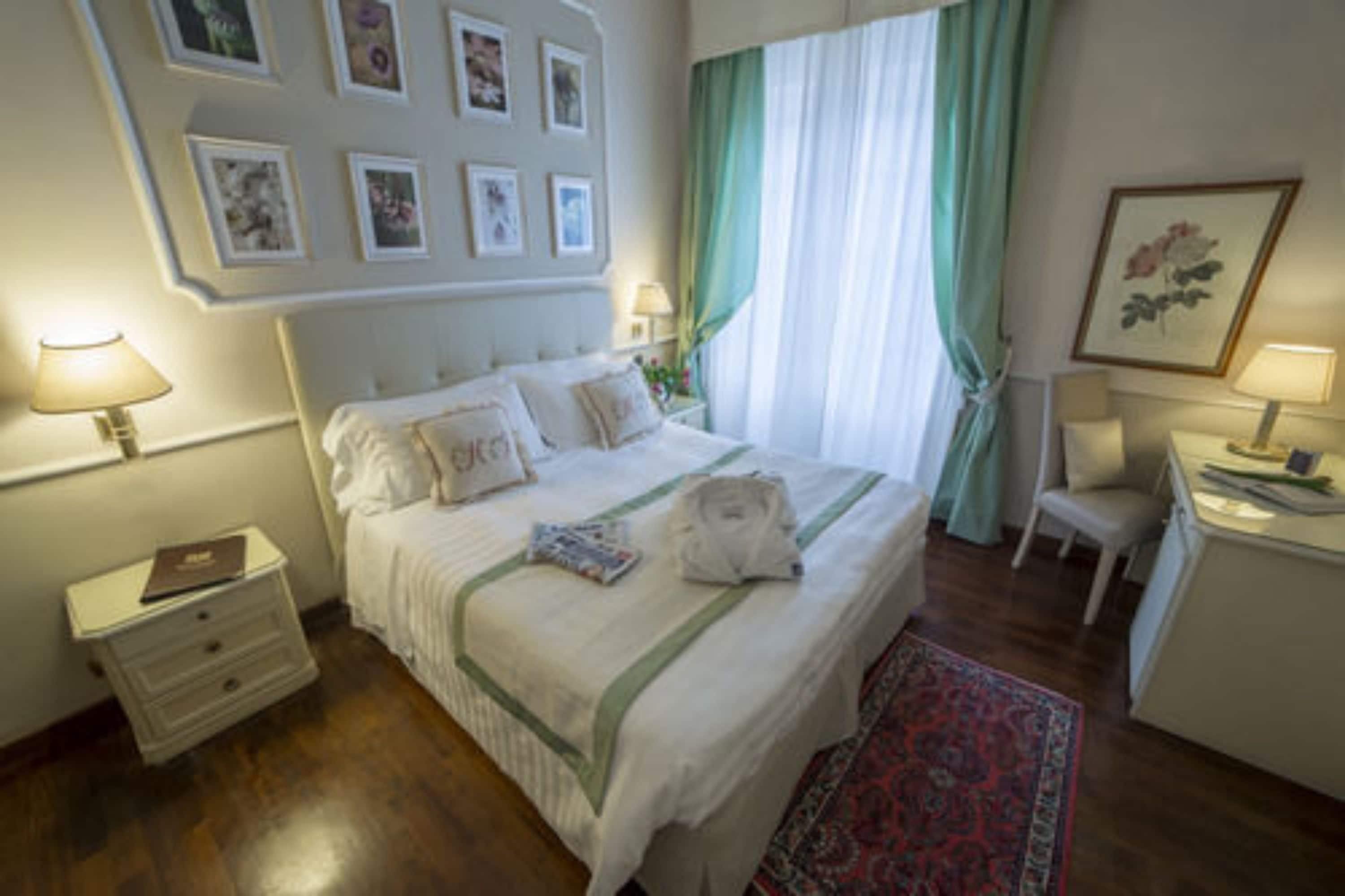 A neatly arranged bedroom with a bed, bedside tables, a nightstand, a desk, and a chair.