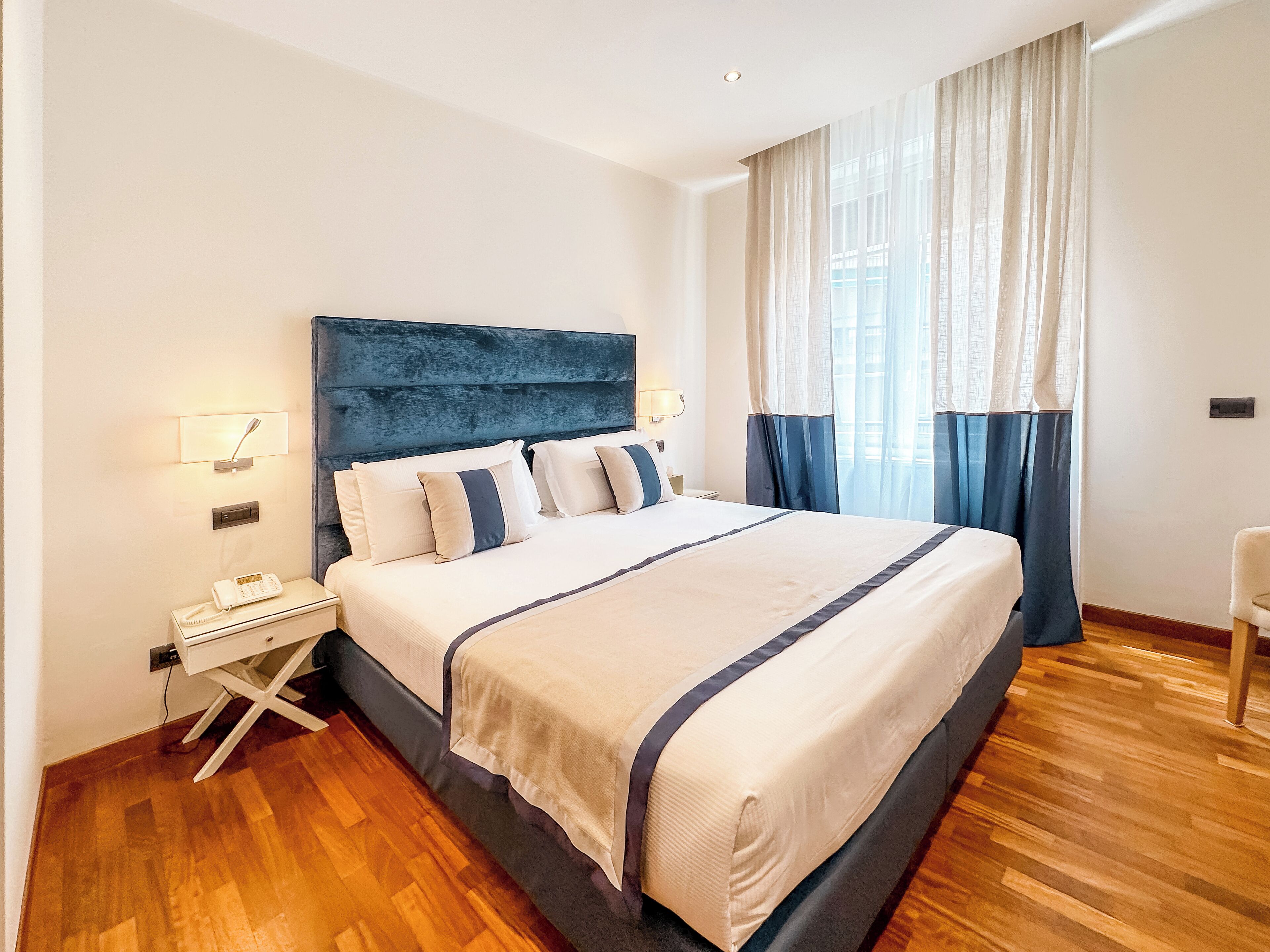 Una camera d'albergo ordinata con un letto grande, lampade sui comodini, un telefono e una finestra con tende.