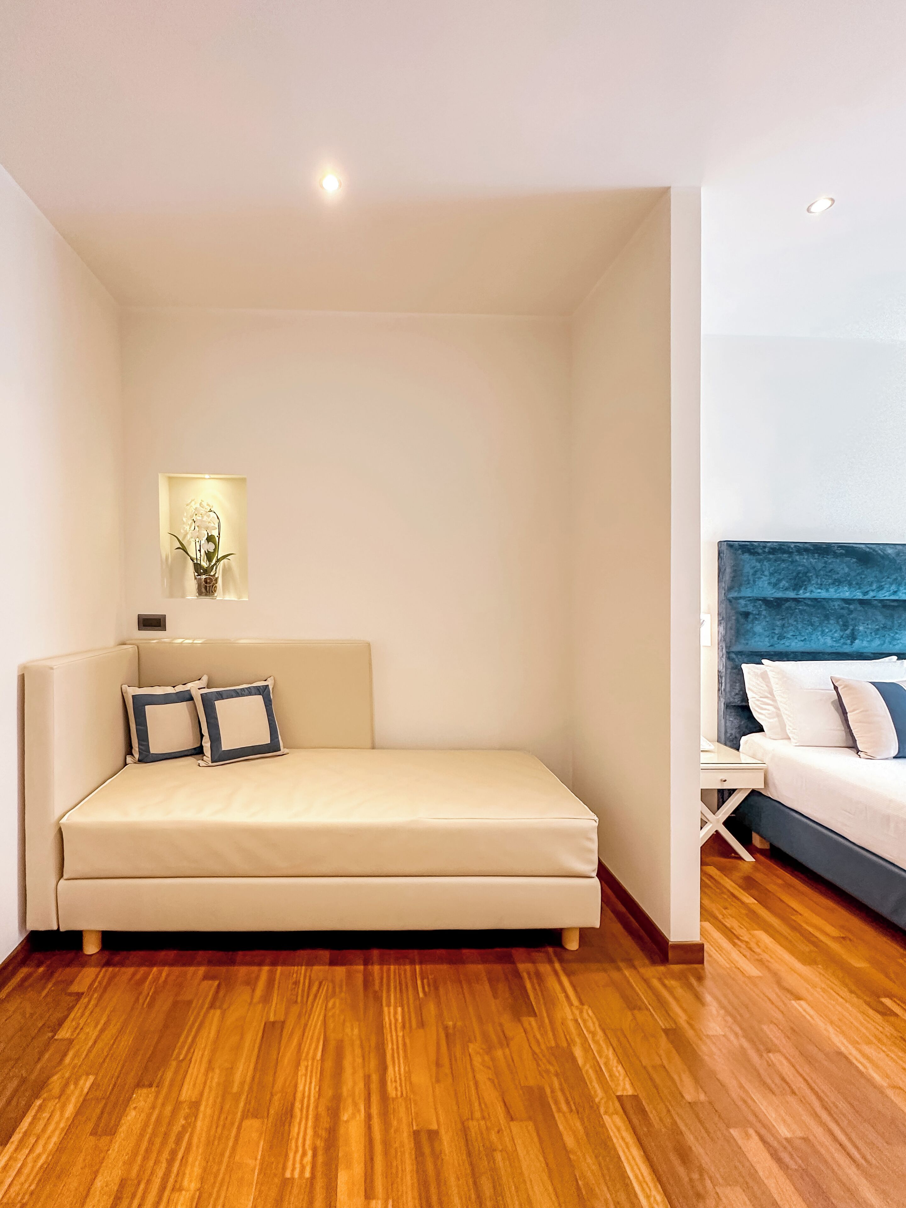 A modern bedroom with a beige sofa, a blue headboard bed, and a wooden floor.
