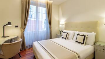 Una habitación de hotel con una cama, un escritorio, una silla, una mesita de noche y una ventana con cortinas.