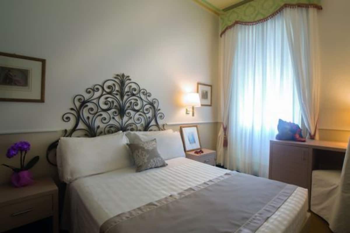 Un lit bien fait, agrémenté d’une tête de lit décorative, une table de chevet avec une lampe et une fenêtre avec des rideaux.