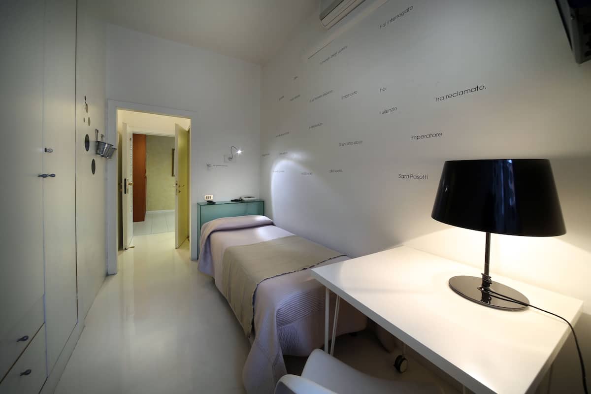 Moderni hotellihuone, jossa on pitkä sänky, yöpöydät, lamppuvarustettu työpöytä ja seinä, jossa on tekstiä.