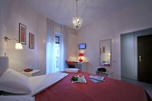 Una habitación de hotel con cama, mesita de noche, lámpara, televisor y puerta.