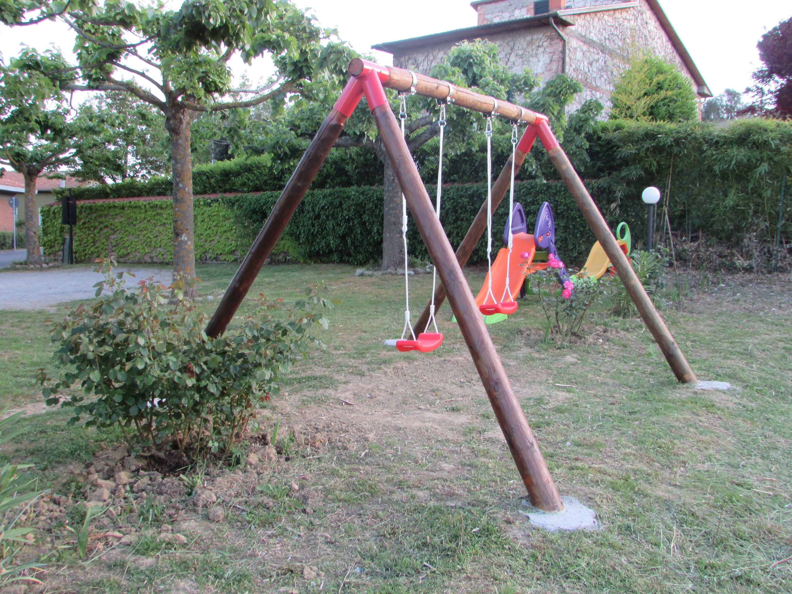 A swing set in a grassy area with trees and a building in the background.