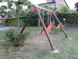 Un ensemble de balançoires installé dans un espace verdoyant, avec des arbres et un bâtiment en arrière-plan.