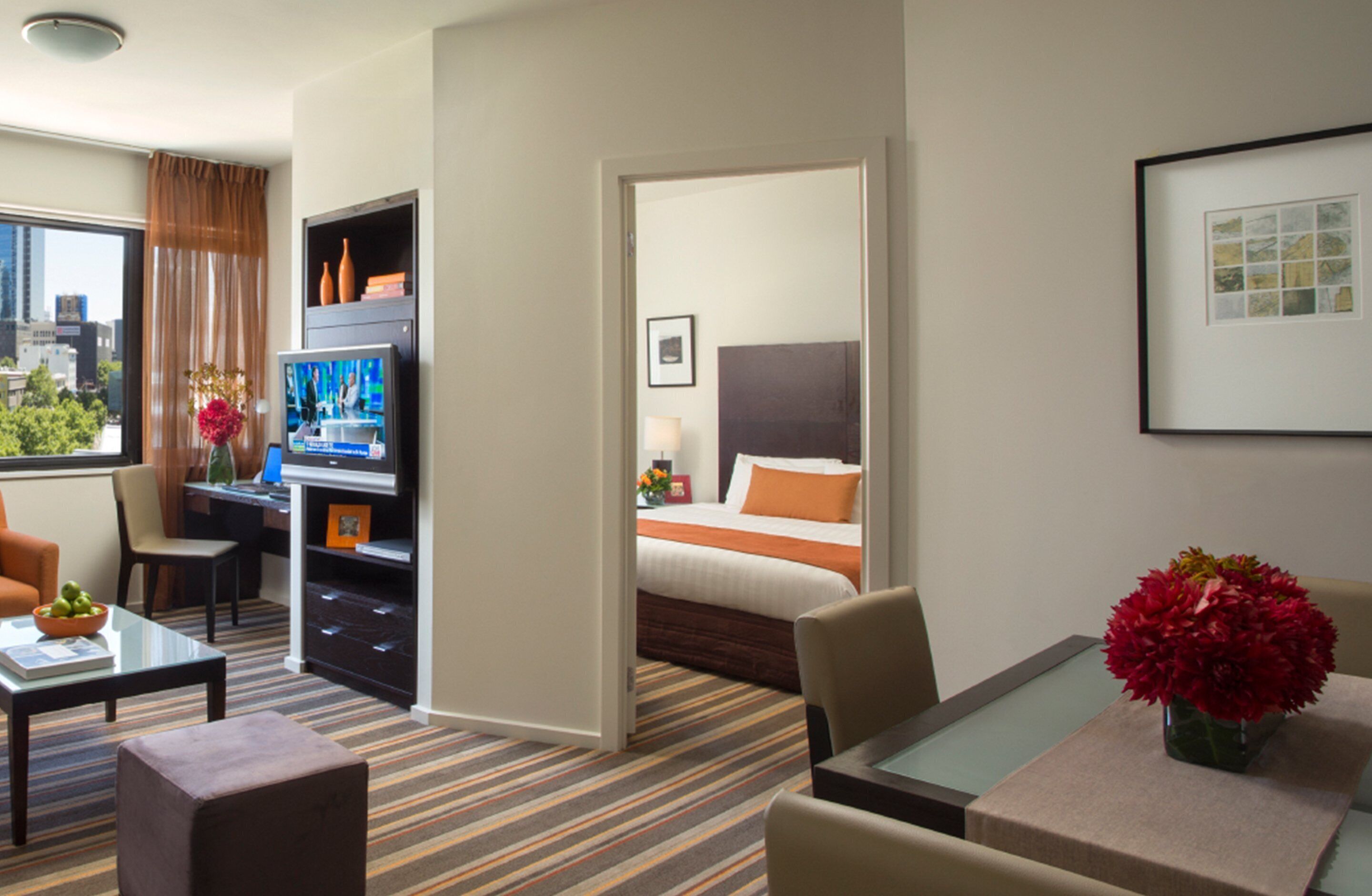 A hotel room with a bed, a desk, a television, a chair, a coffee table, and a view of the city.