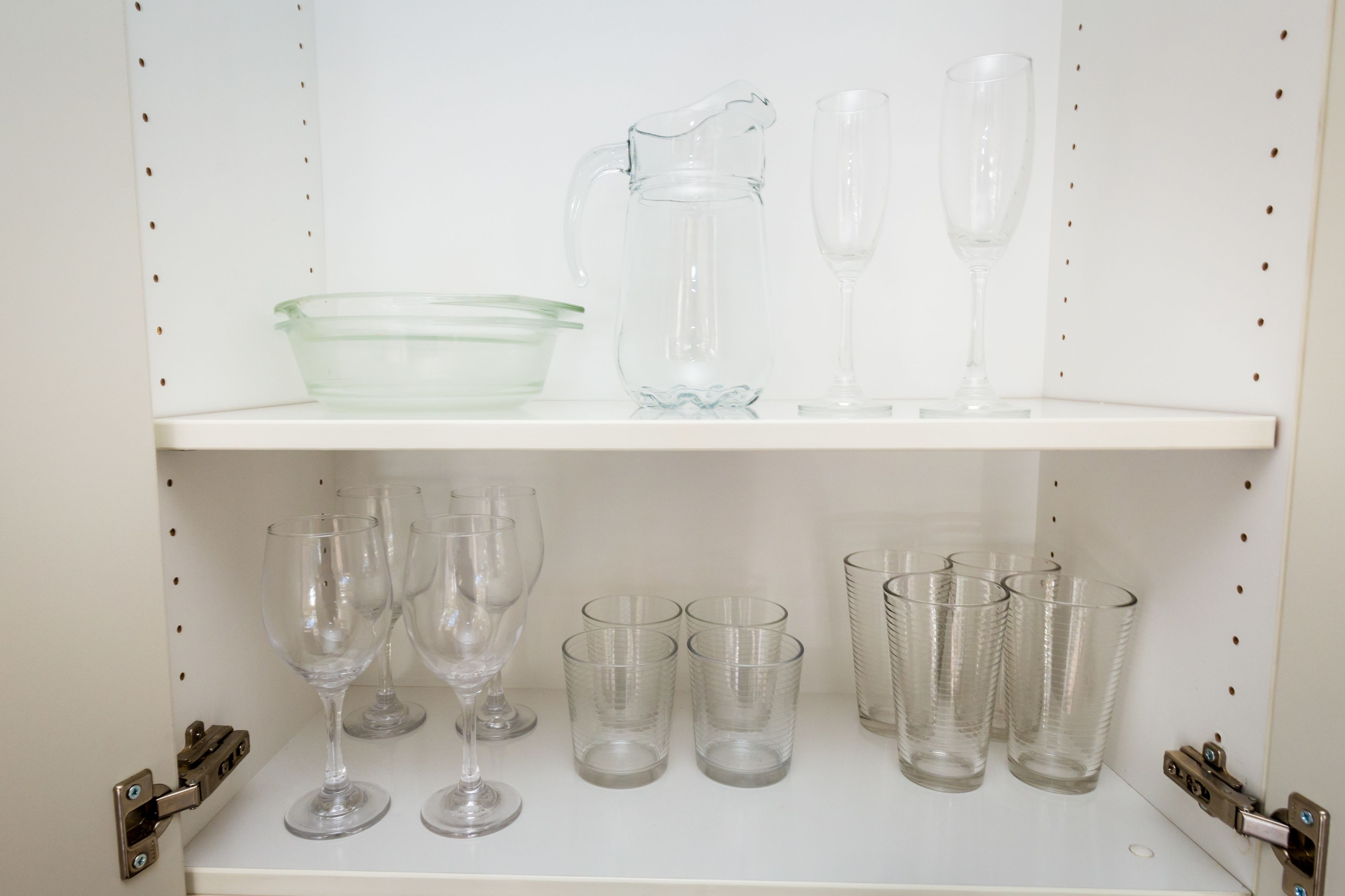 A shelf with various glassware including a pitcher, wine glasses, and multiple cups.