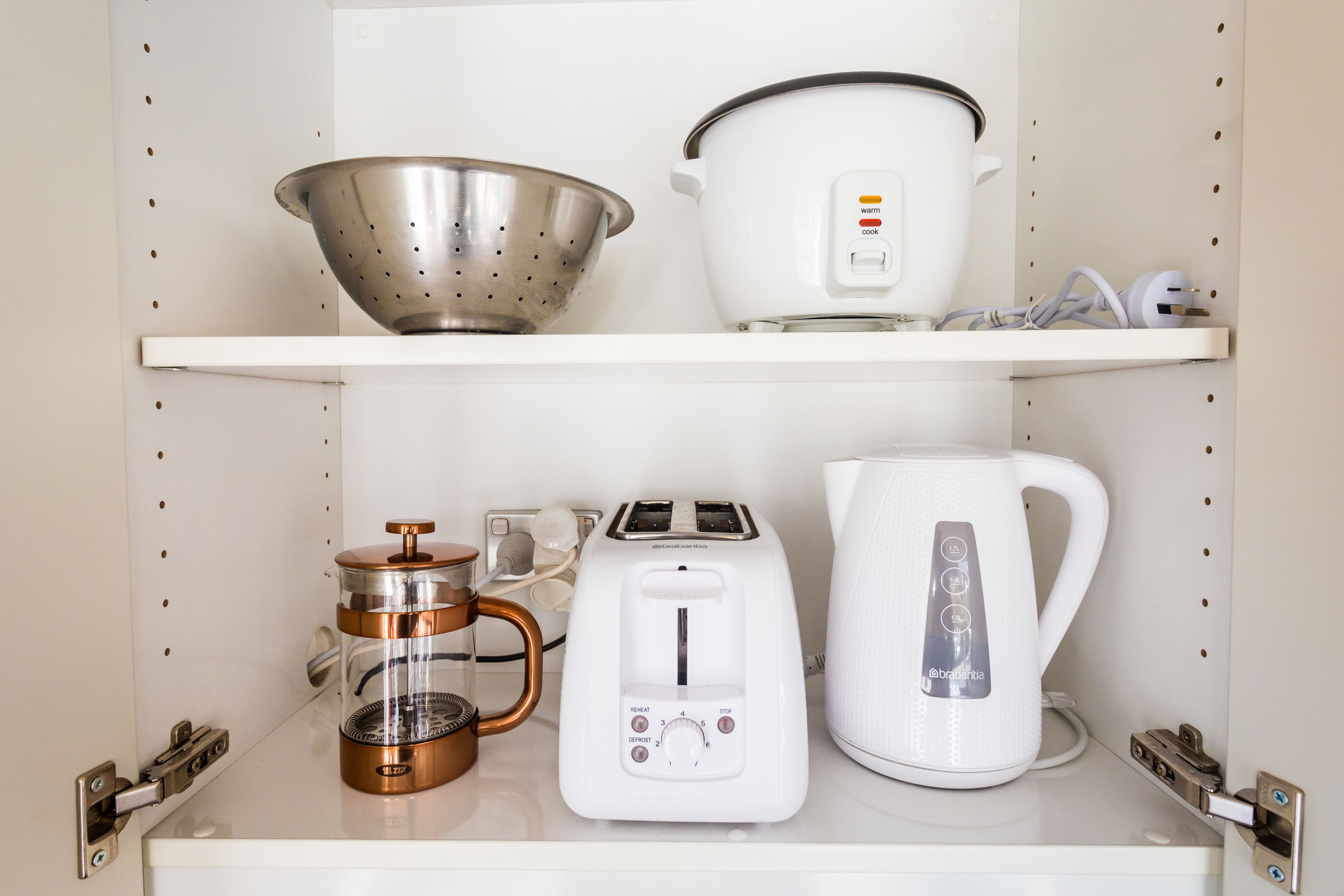 Una estantería en la cocina con un colador, una olla de cocción lenta, una cafetera, un tostador y un hervidor.