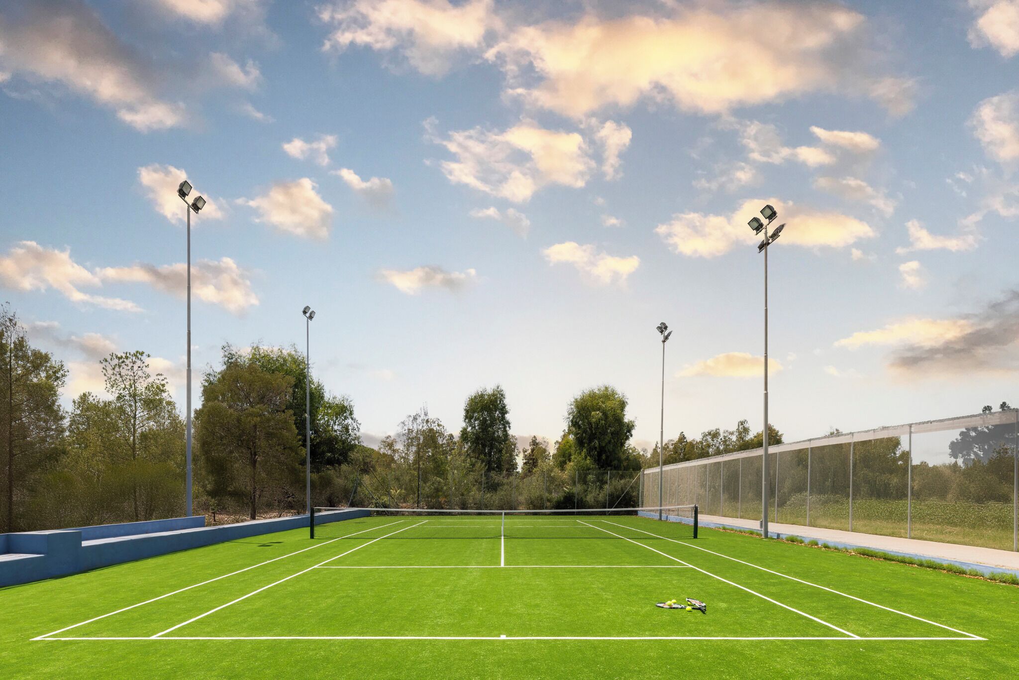 Un court de tennis avec un filet, entouré d’arbres et d’une clôture.