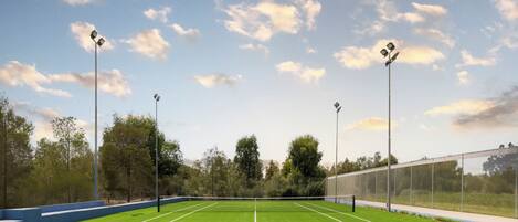 Cancha de tenis con red, rodeada de árboles y una valla.