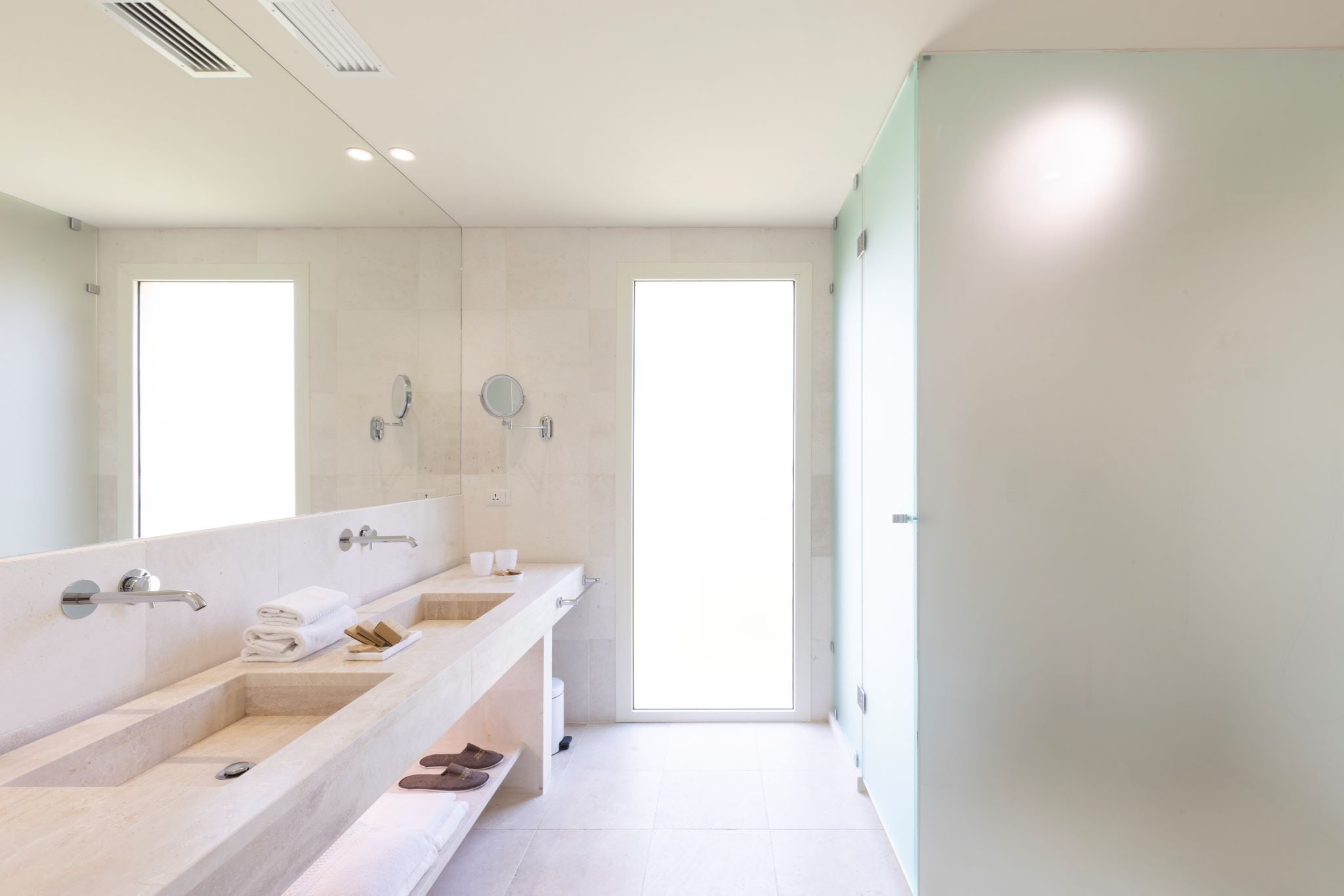 Un baño moderno con dos lavabos, un espejo grande y una puerta que da a una habitación luminosa.