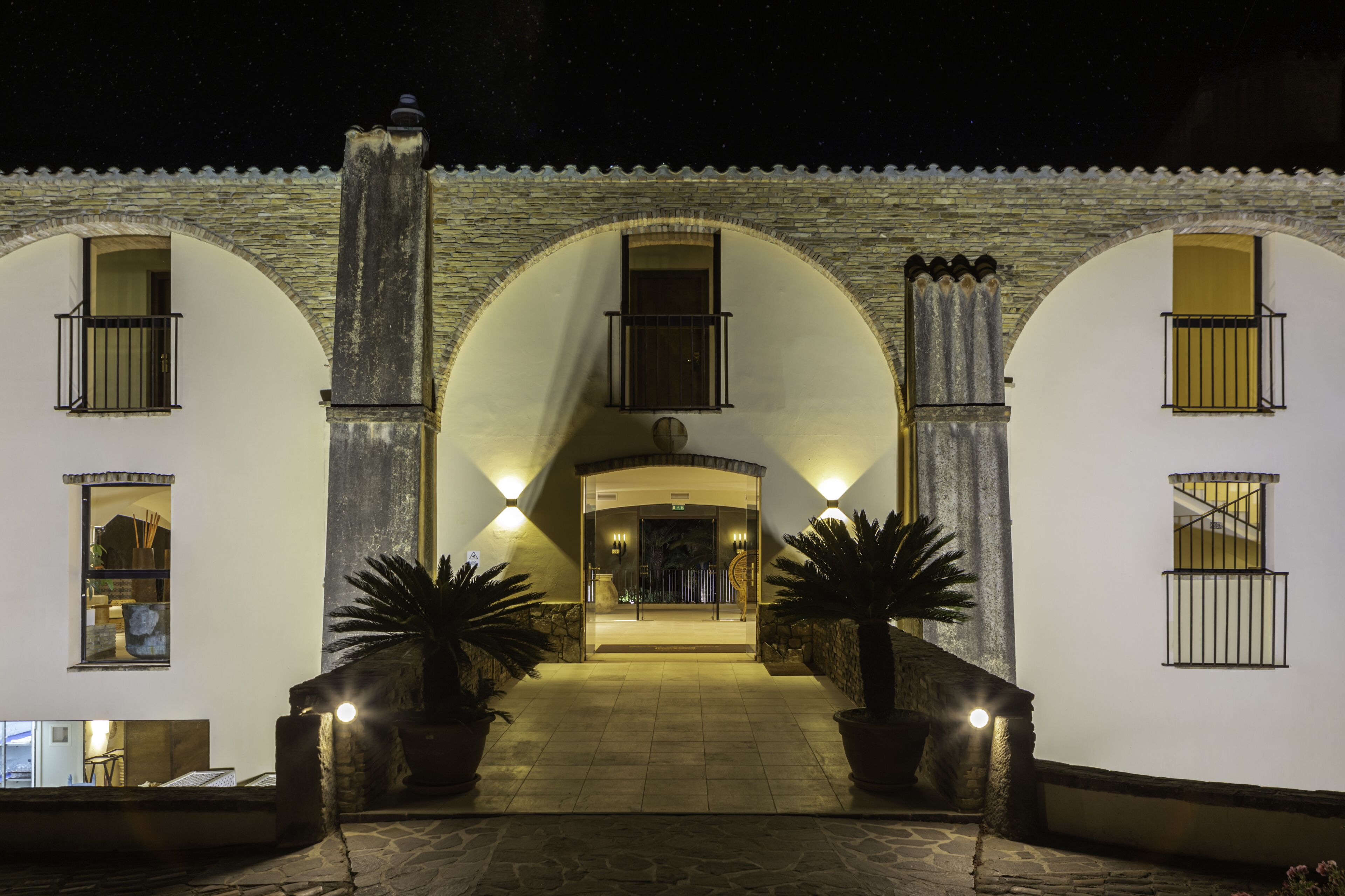A hotel entrance with a stone facade, arched windows, and potted plants.