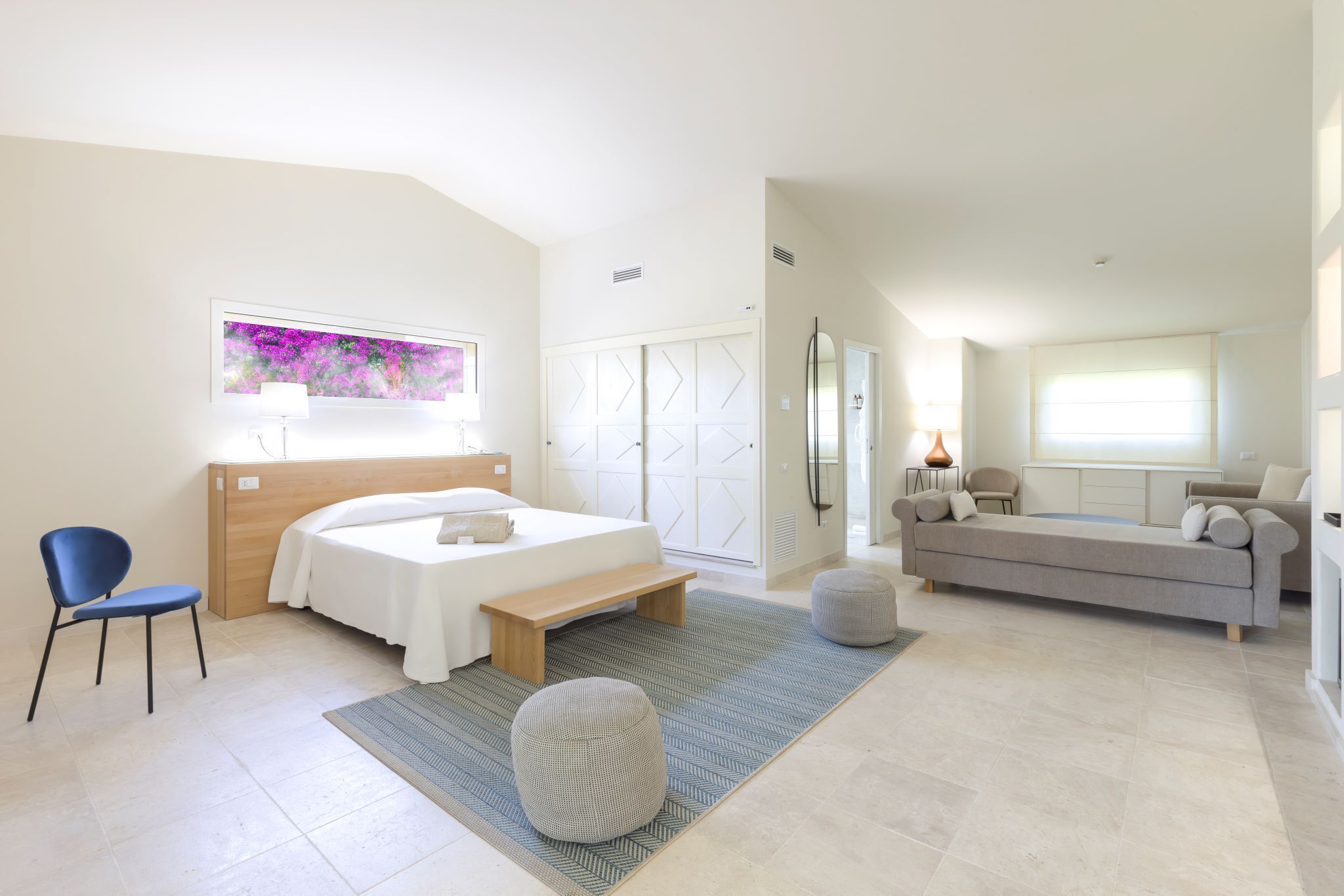 Une chambre à coucher moderne avec un lit, une table de chevet, une chaise et un canapé dans l’espace de vie adjacent.