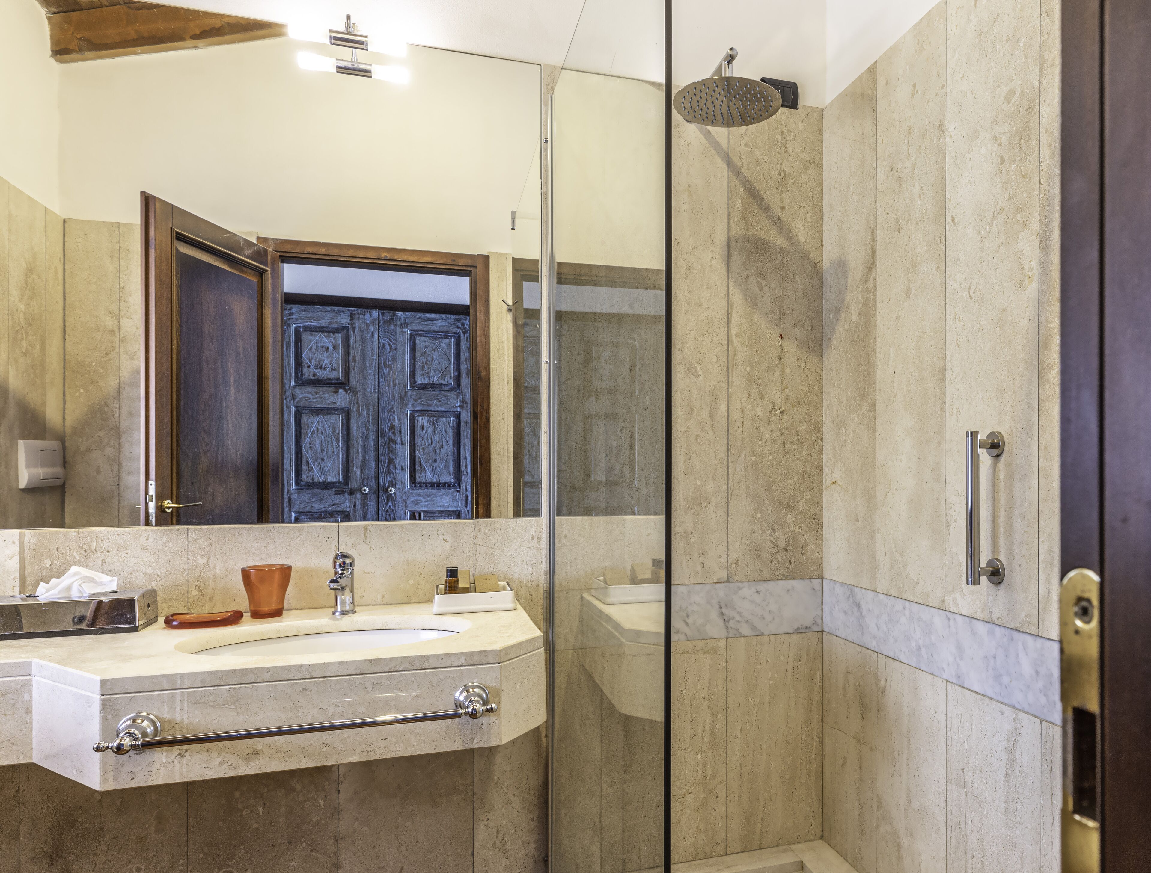 A modern bathroom with a glass-enclosed shower, a large mirror, and a wooden door.