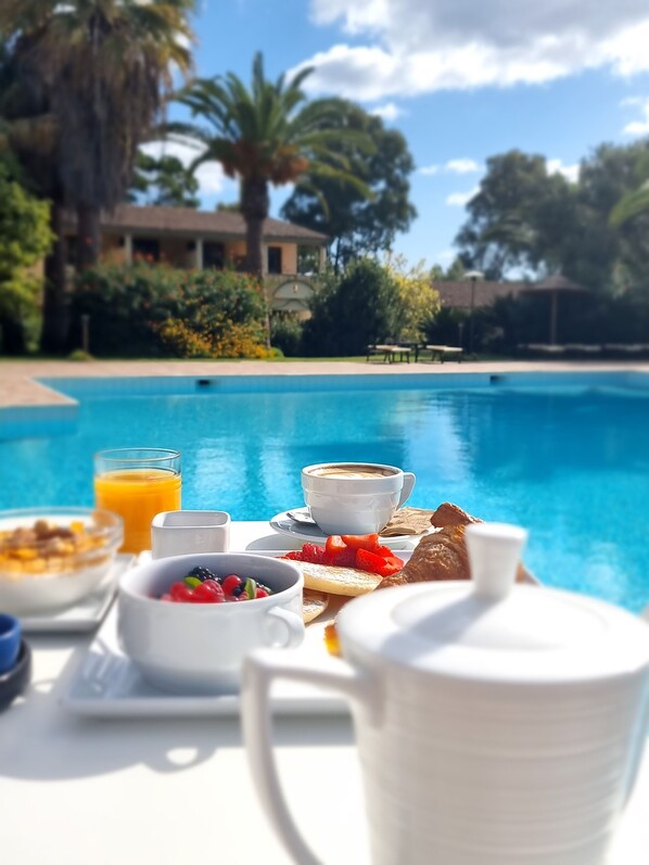 A breakfast setup by a pool with a clear view of the pool and surrounding greenery. - Hotel Costa Dei Fiori (Pula)