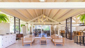 A spacious indoor area with wooden furniture, a high ceiling, and a view through glass doors to an outdoor garden. - Hotel Costa Dei Fiori (Pula)