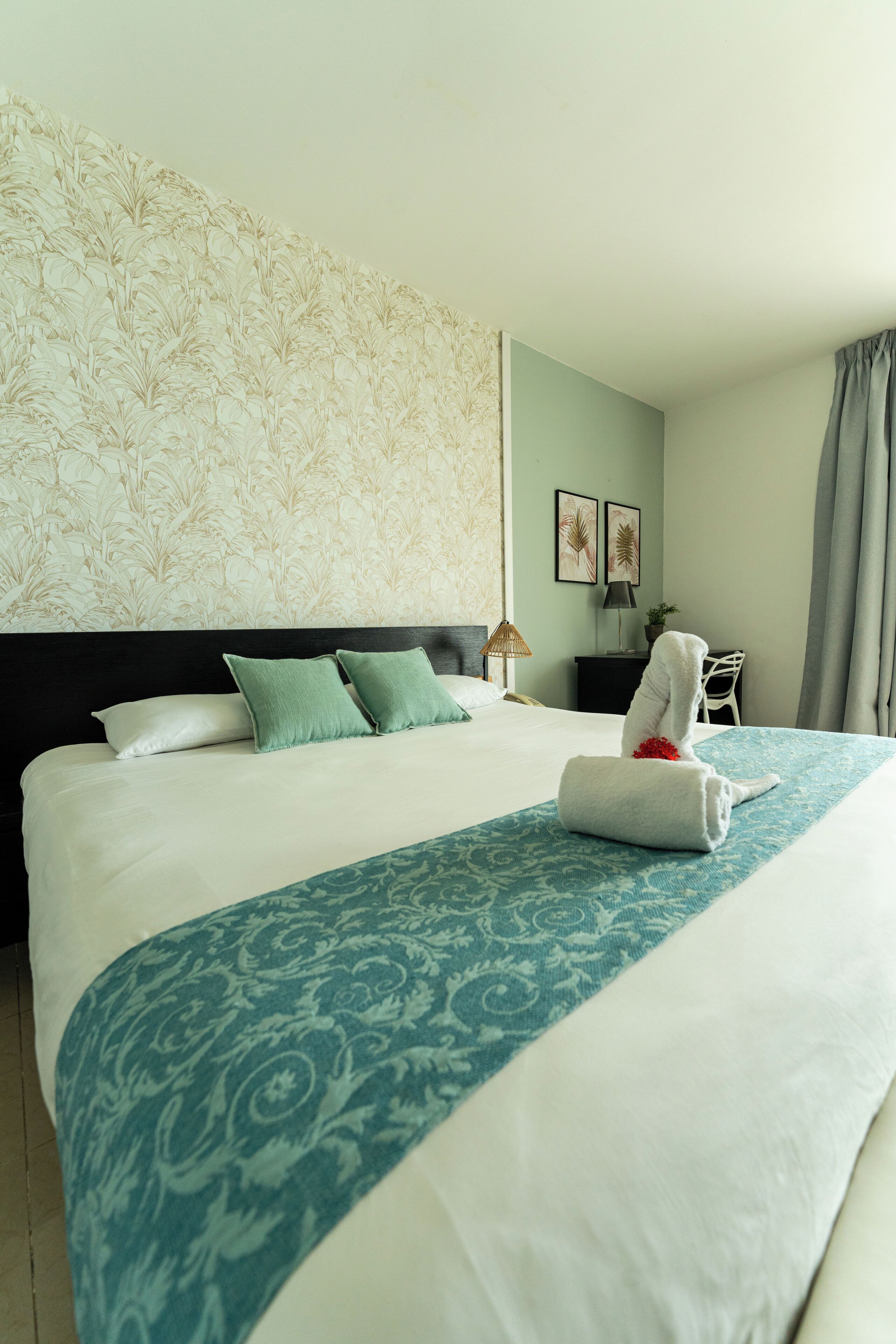 Una habitación de hotel con una cama grande, un cabecero, una mesita de noche, una lámpara, una silla y una ventana con cortinas.