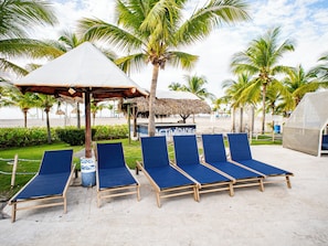 A beachside lounge area with sun loungers and a thatched-roof structure.
