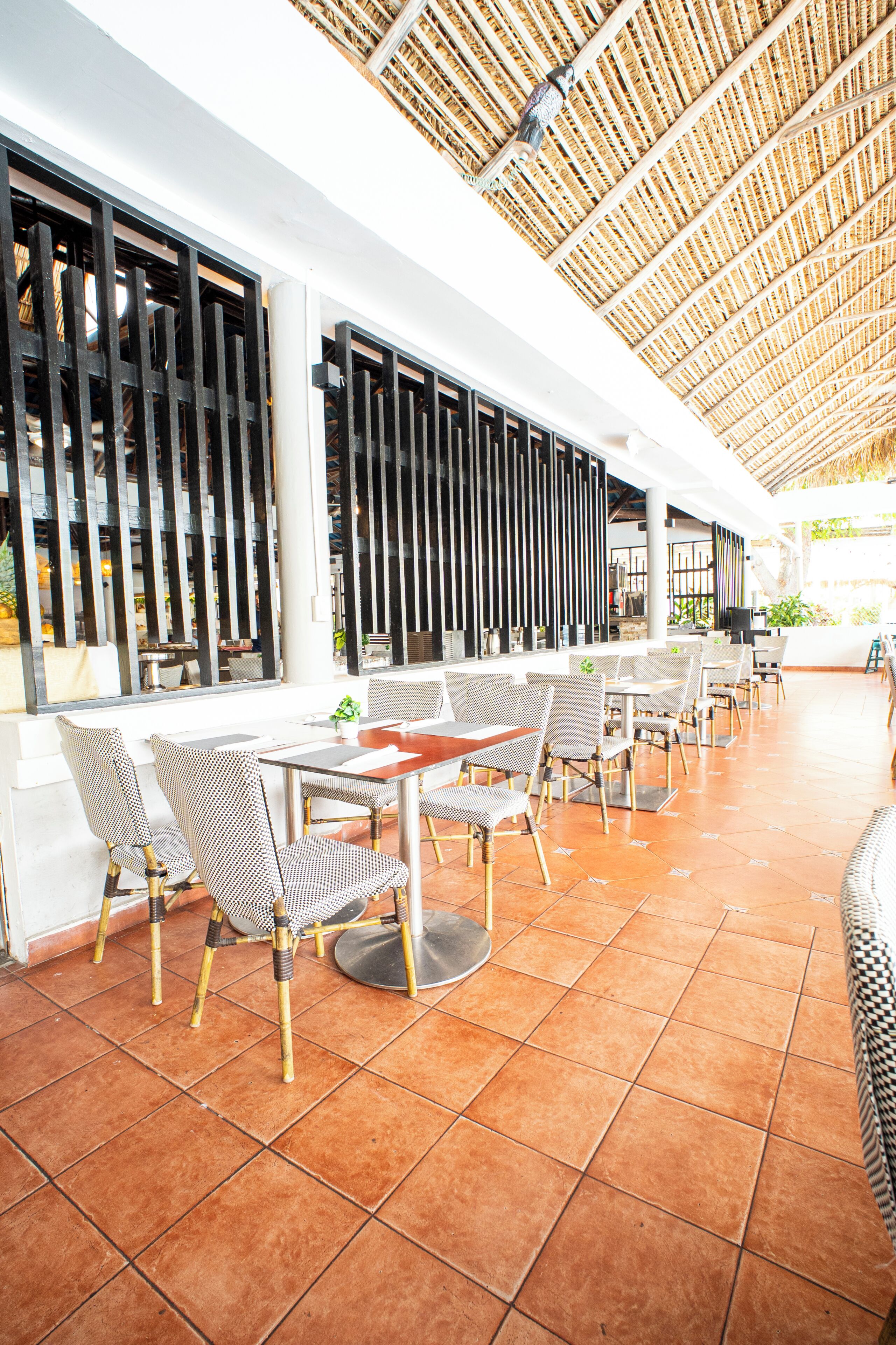 Un restaurante con terraza, mesas y sillas, bajo un techo de paja.
