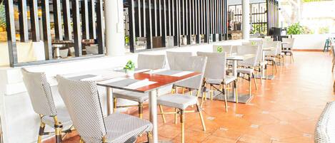 Un restaurante con terraza, mesas y sillas, bajo un techo de paja.