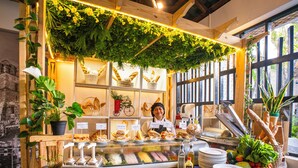 A bakery counter with bread, sandwiches, and a display case, surrounded by plants and wooden shelves. - Playa Blanca Beach Resort - All Inclusive (Rio Hato)