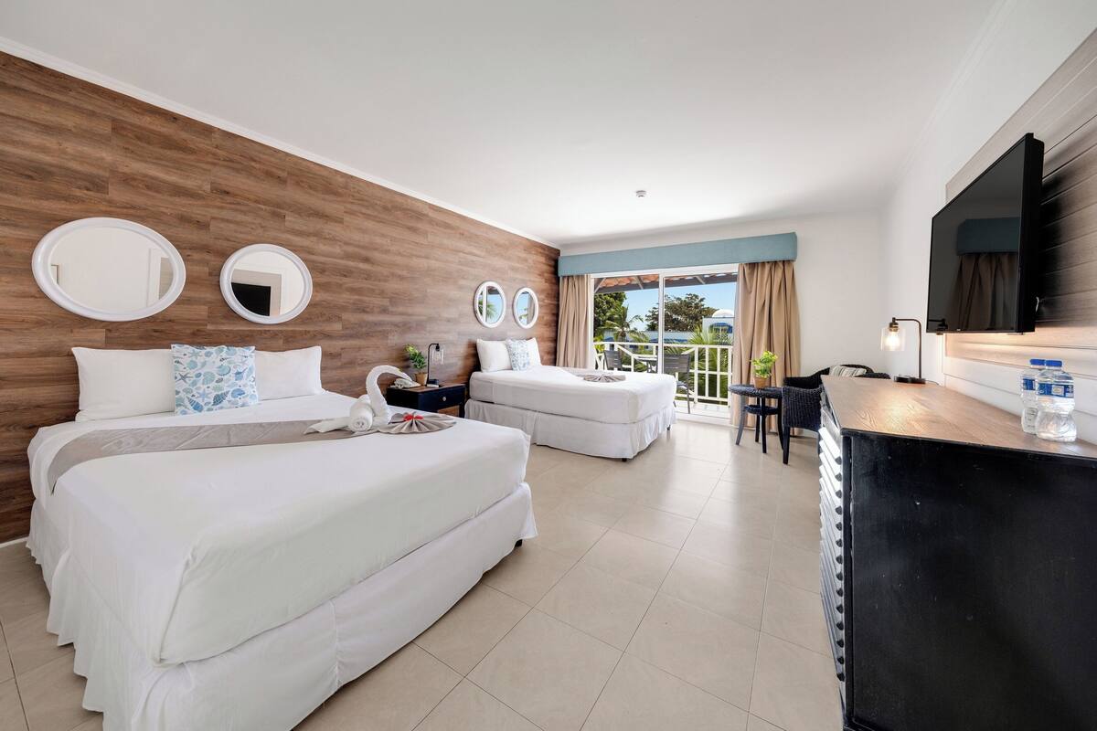 A hotel room with two beds, a desk, a TV, and a balcony with a view.