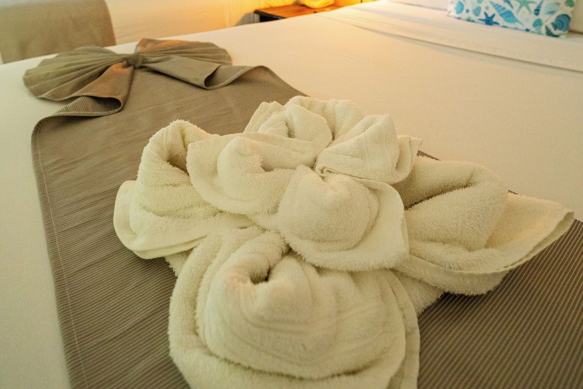 A hotel room with a neatly made bed, a bedside table with a towel, and a wooden headboard.