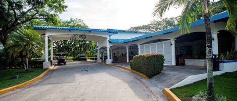 Un estacionamiento techado con un vehículo, palmeras y un edificio con techo azul.
