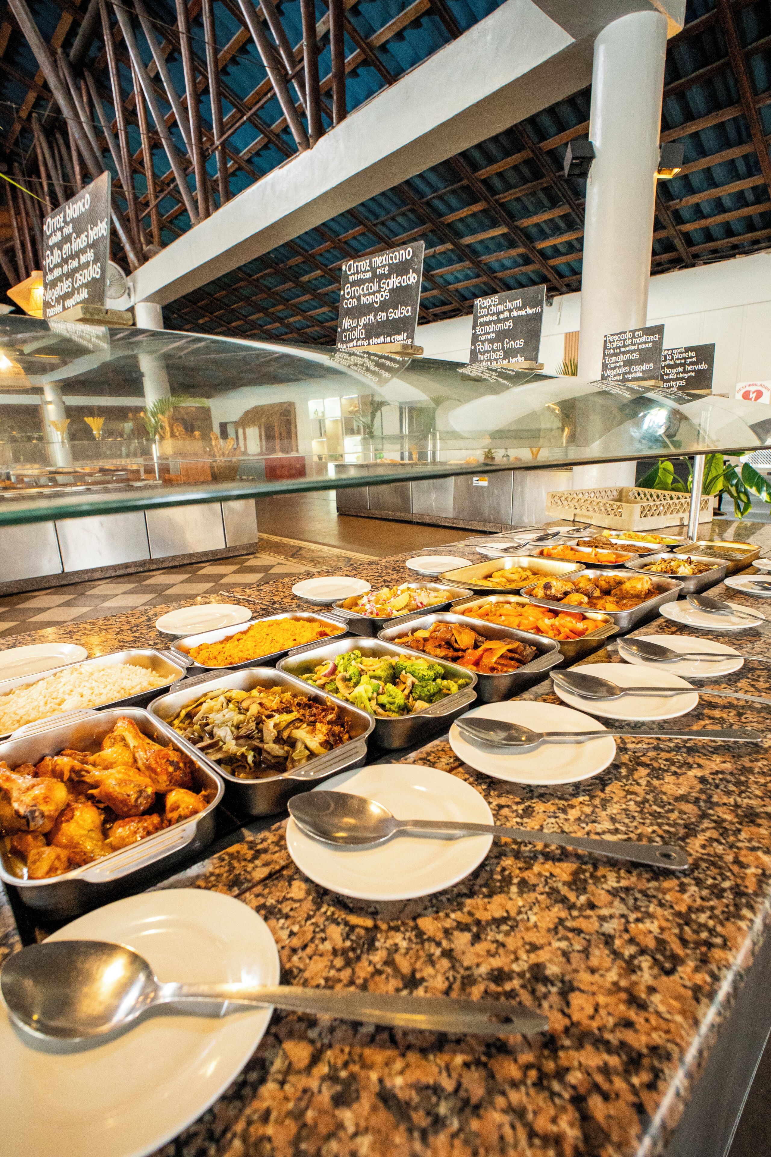 A buffet with various food options, a glass display case, and a high ceiling with visible beams.