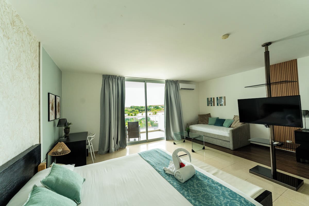 A hotel room with a bed, a TV, a sofa, a desk, and a view of the outdoors.