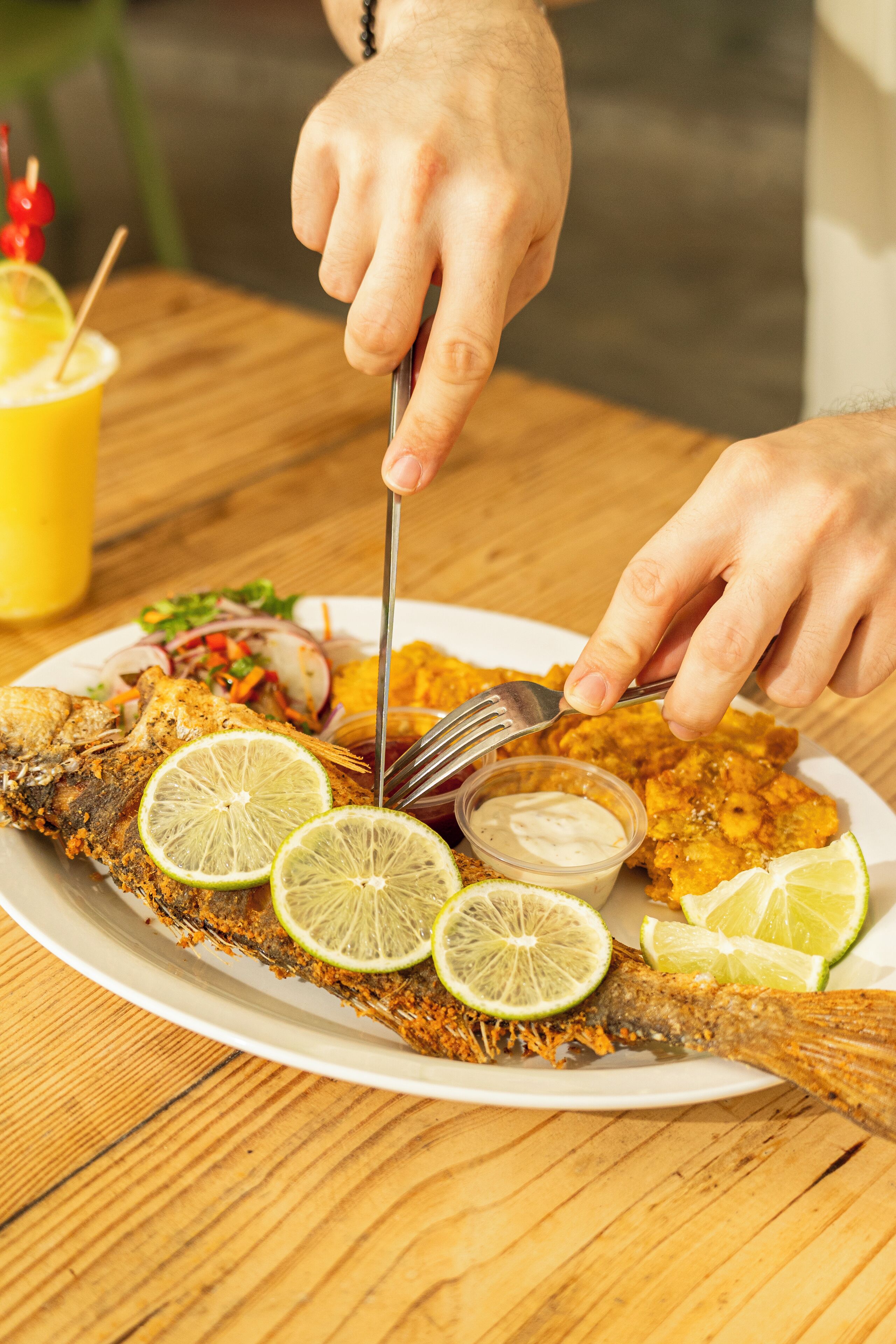 Eine Person schneidet einen Fisch auf einem Teller mit Limettenscheiben und einer Beilage Soße.
